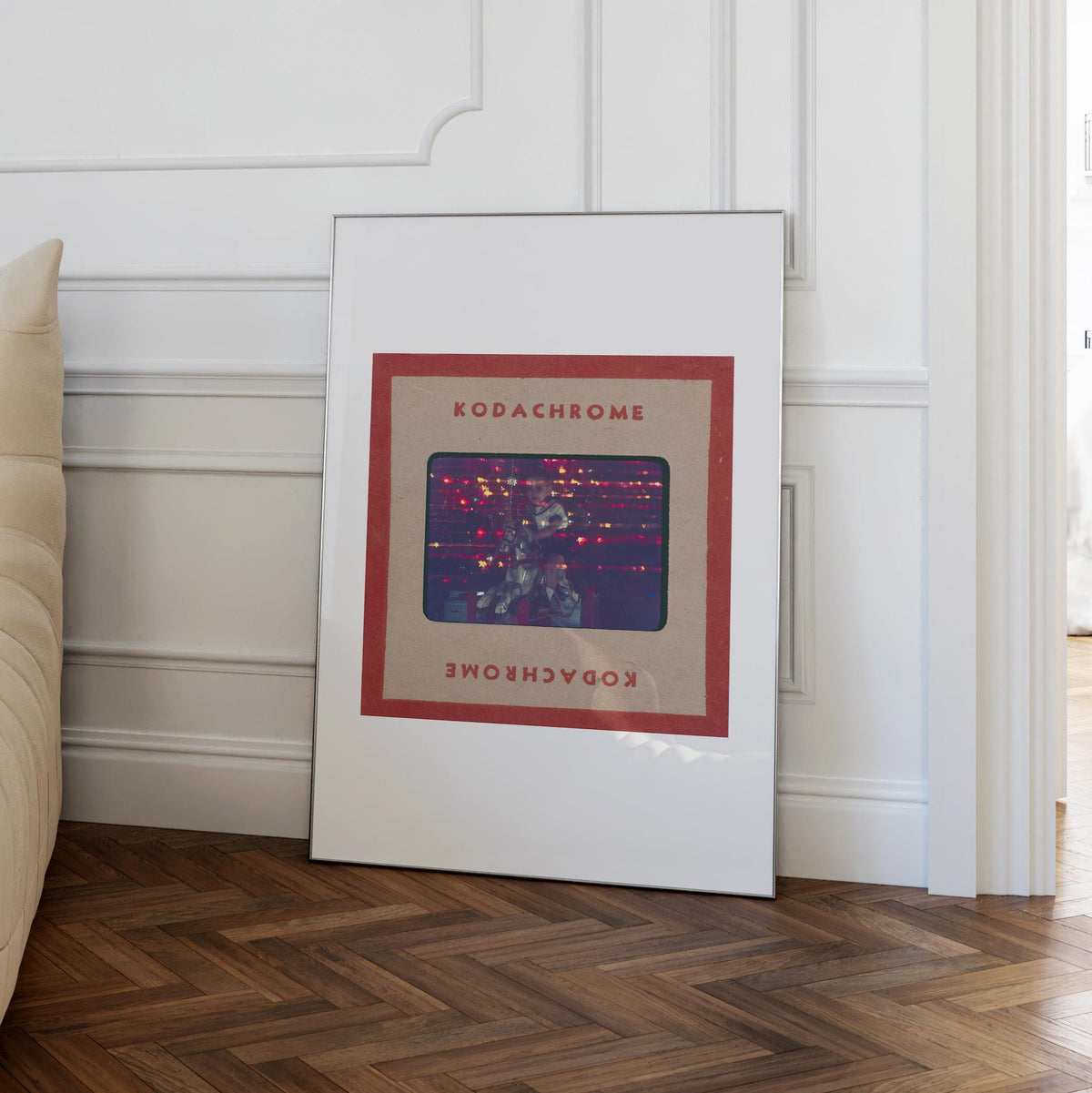 a framed artwork titled "Kodachrome" on a white wall, with a wooden floor beneath it.
