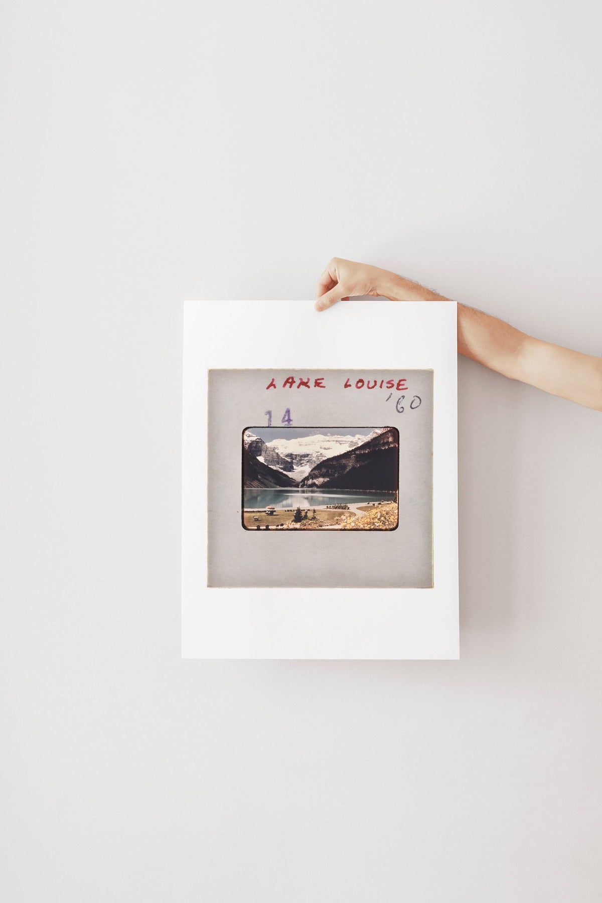 A person's hand is holding a framed photograph of a mountain landscape.