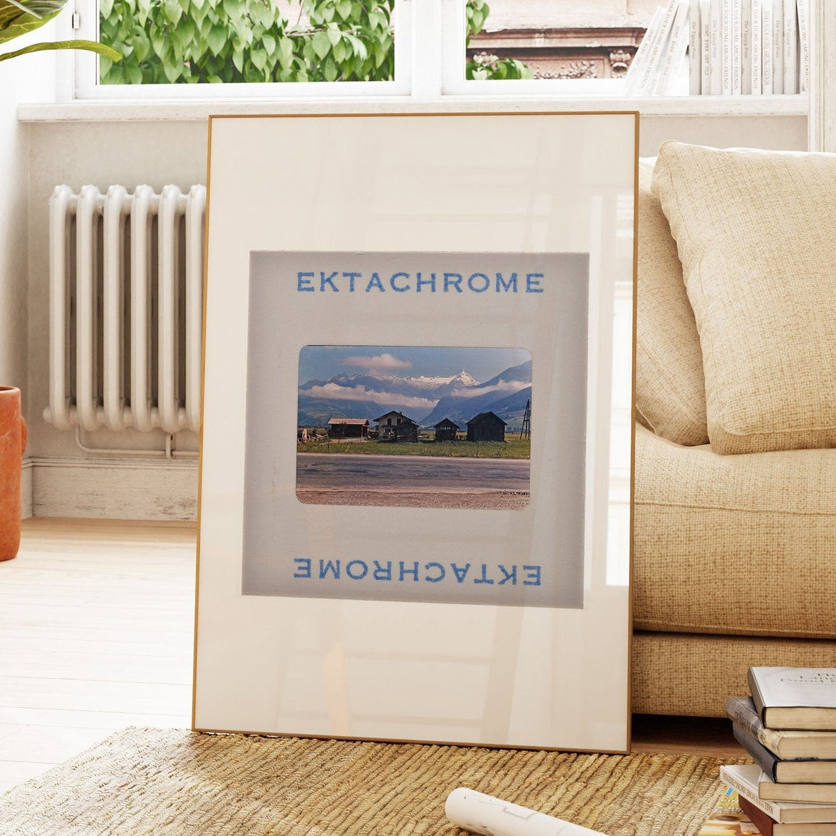 a framed photograph of a rural landscape with mountains in the background, placed on a wooden floor in a living room setting.