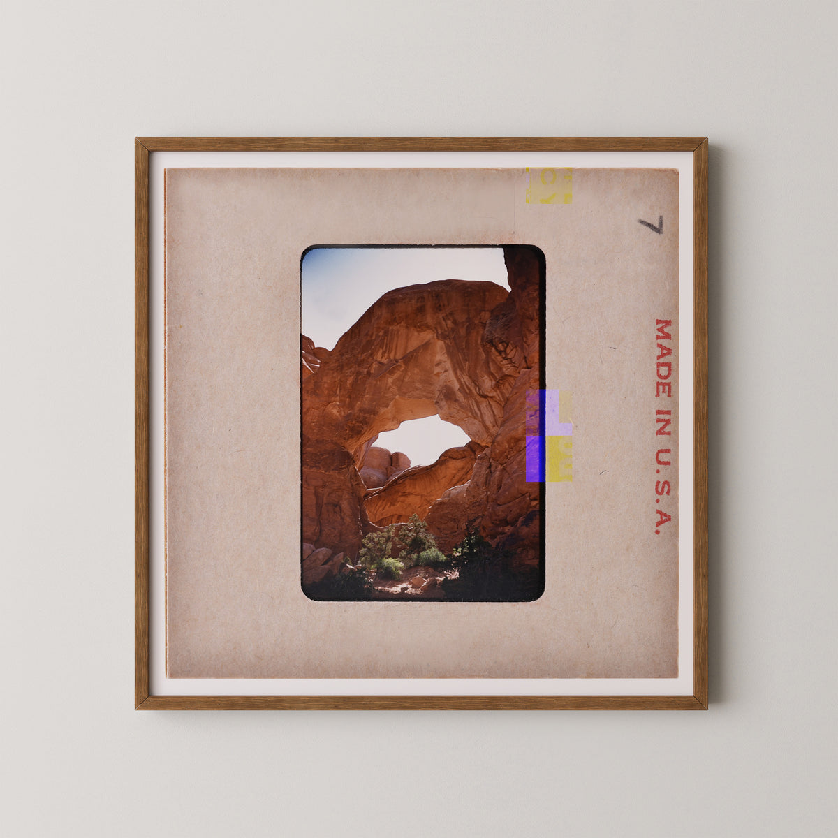 The image is a framed photograph of a desert landscape with a large rock formation, likely a canyon or arch, in the background.