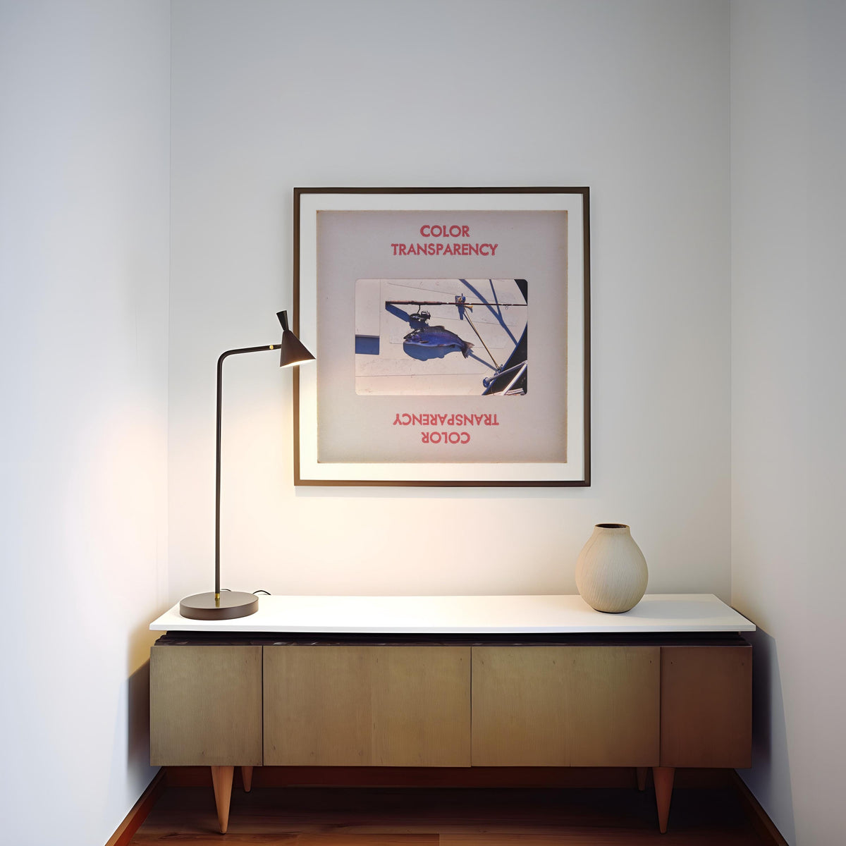 a minimalist interior design with a white wall, a wooden cabinet, a lamp, and a framed poster.
