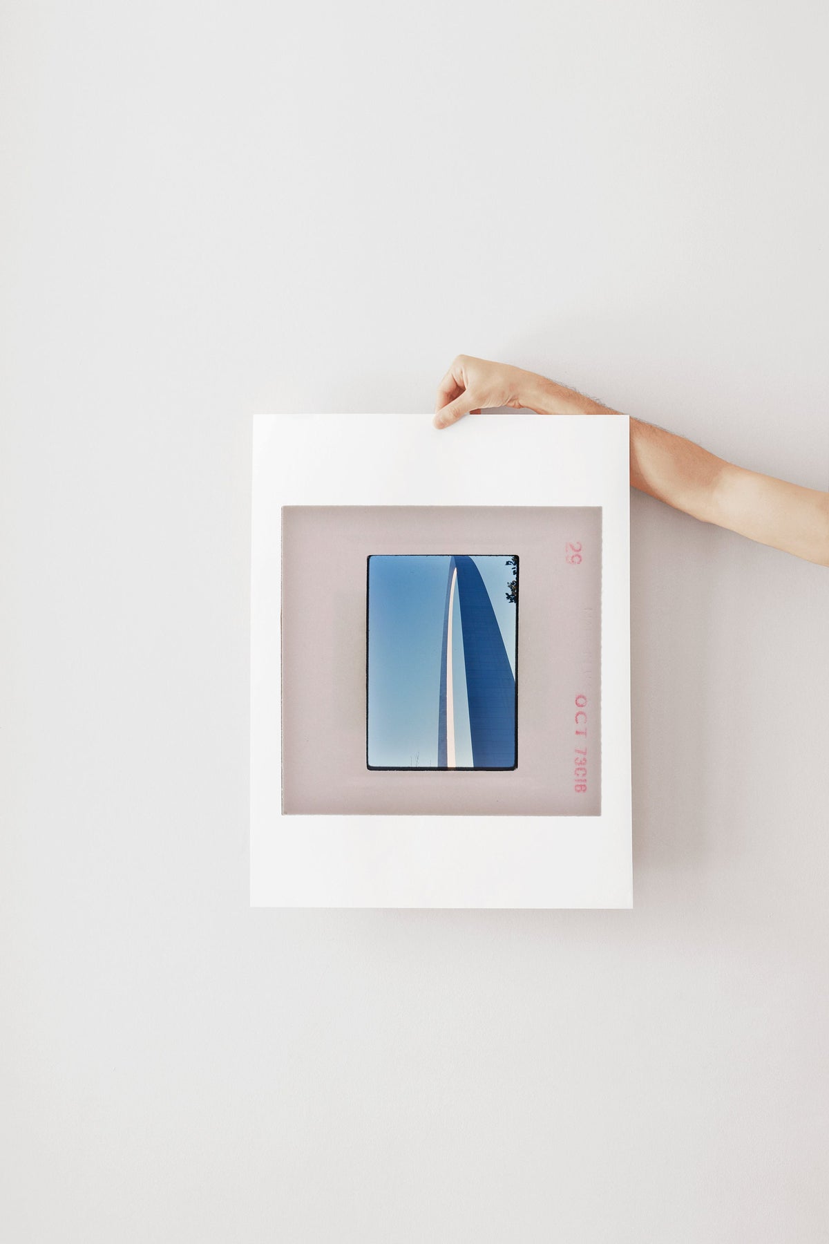 A person's hand is holding a white frame with a framed image of a sailboat in the background.
