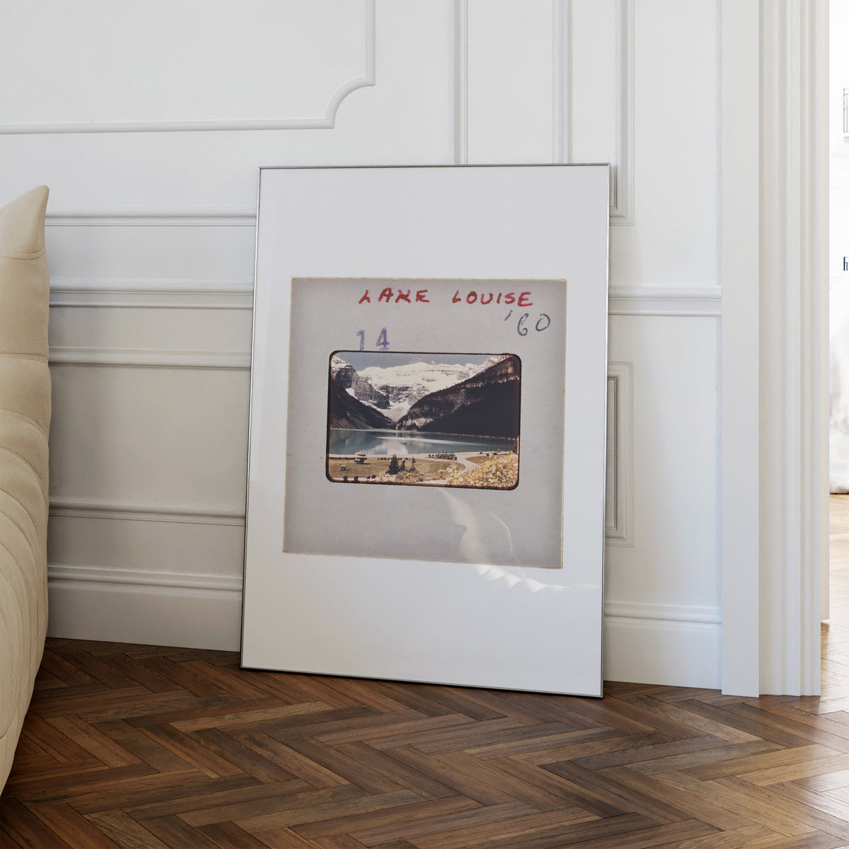 A framed photograph of a mountain landscape is leaning against a white wall in a room with a wooden floor.