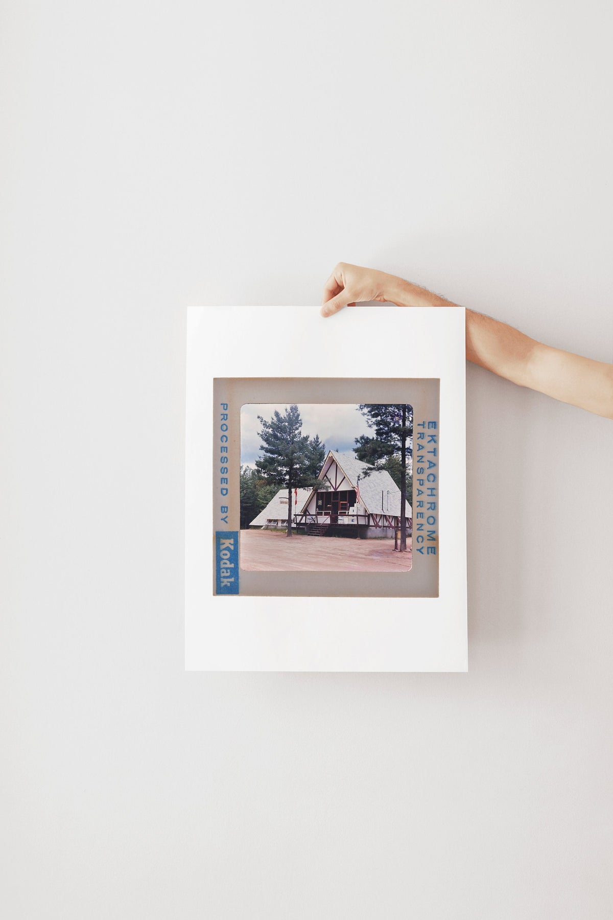 A person's hand is holding a framed photograph of a building with a tree in the background.