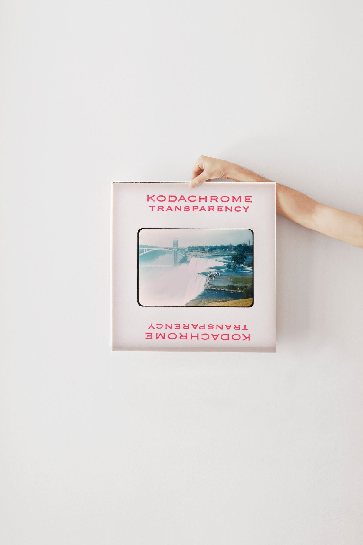 A hand is holding a framed photograph of a waterfall, with the text "KODACHrome Transparency" visible on the frame.