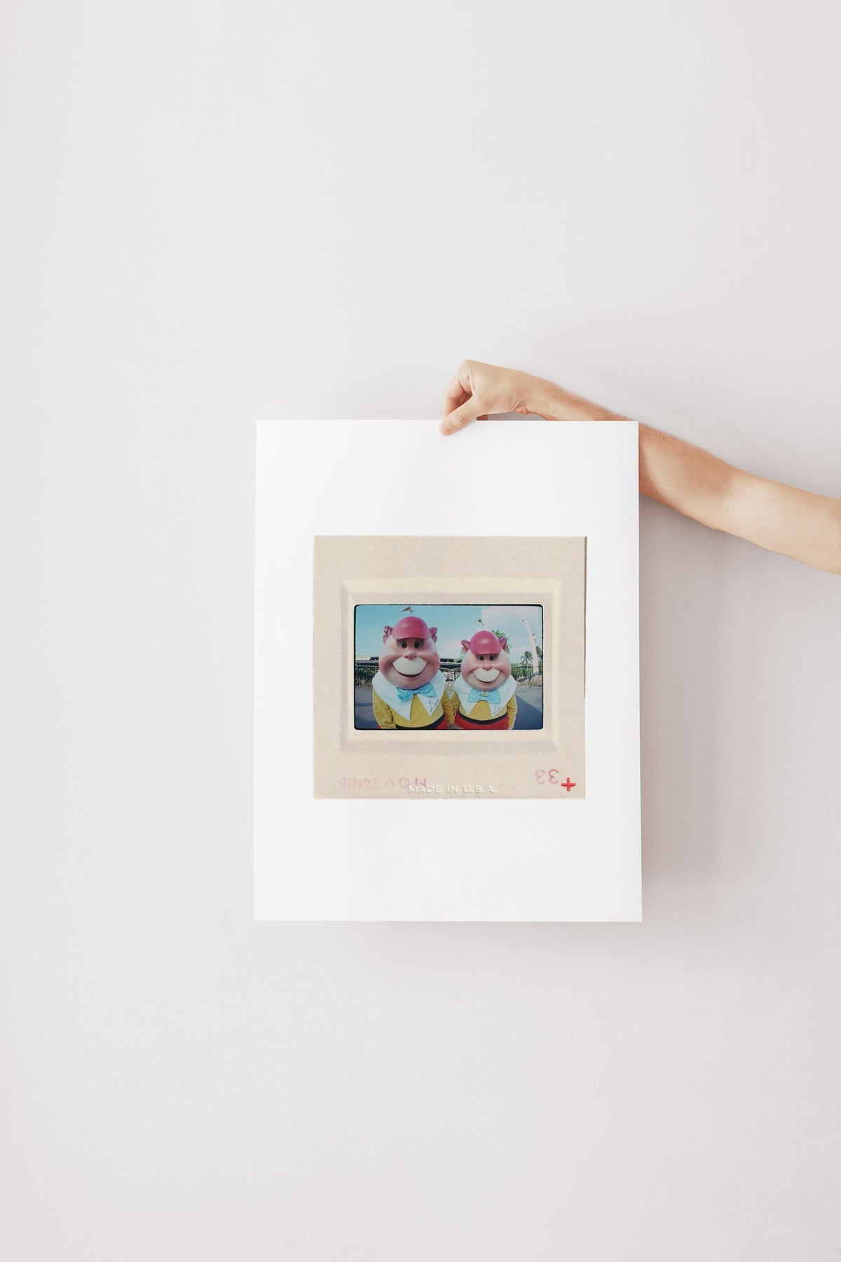 A person's hand is holding a white picture frame with a framed image of two cartoon characters inside it.