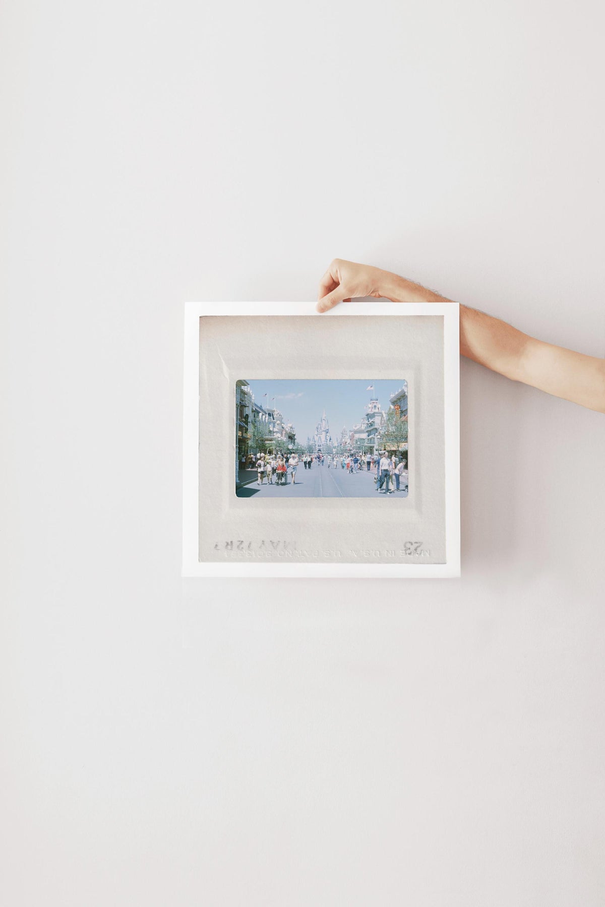 A person's hand is holding a white picture frame with a framed photograph of a city street scene inside it.