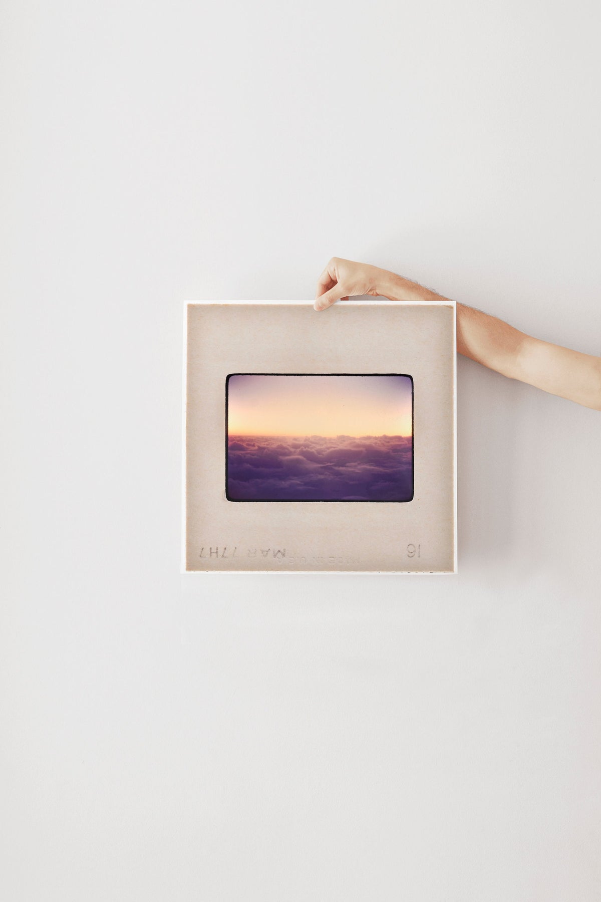 A person's hand is holding a framed picture of a sunset over a body of water.