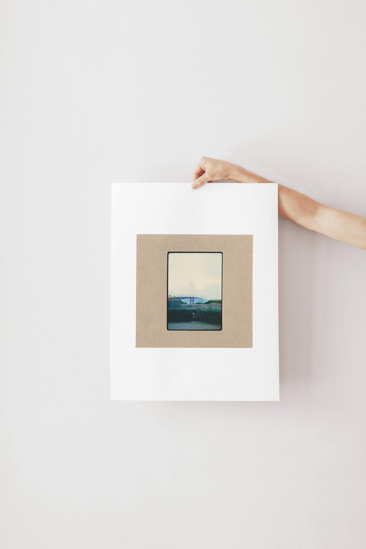 Vintage 35mm slide photograph of the Golden Gate Bridge partially obscured by dense fog, with only the tower visible above the cloud layer, viewed from a concrete overlook with green hedges in the foreground. Printed as a giclée fine art print on archival matte paper.