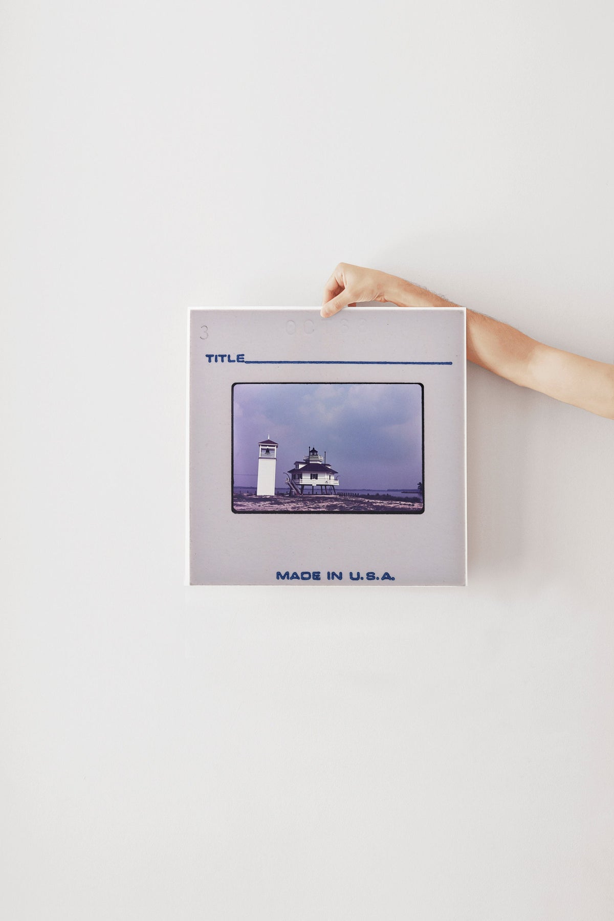 A person's hand is holding a framed photograph of a lighthouse against a white background.