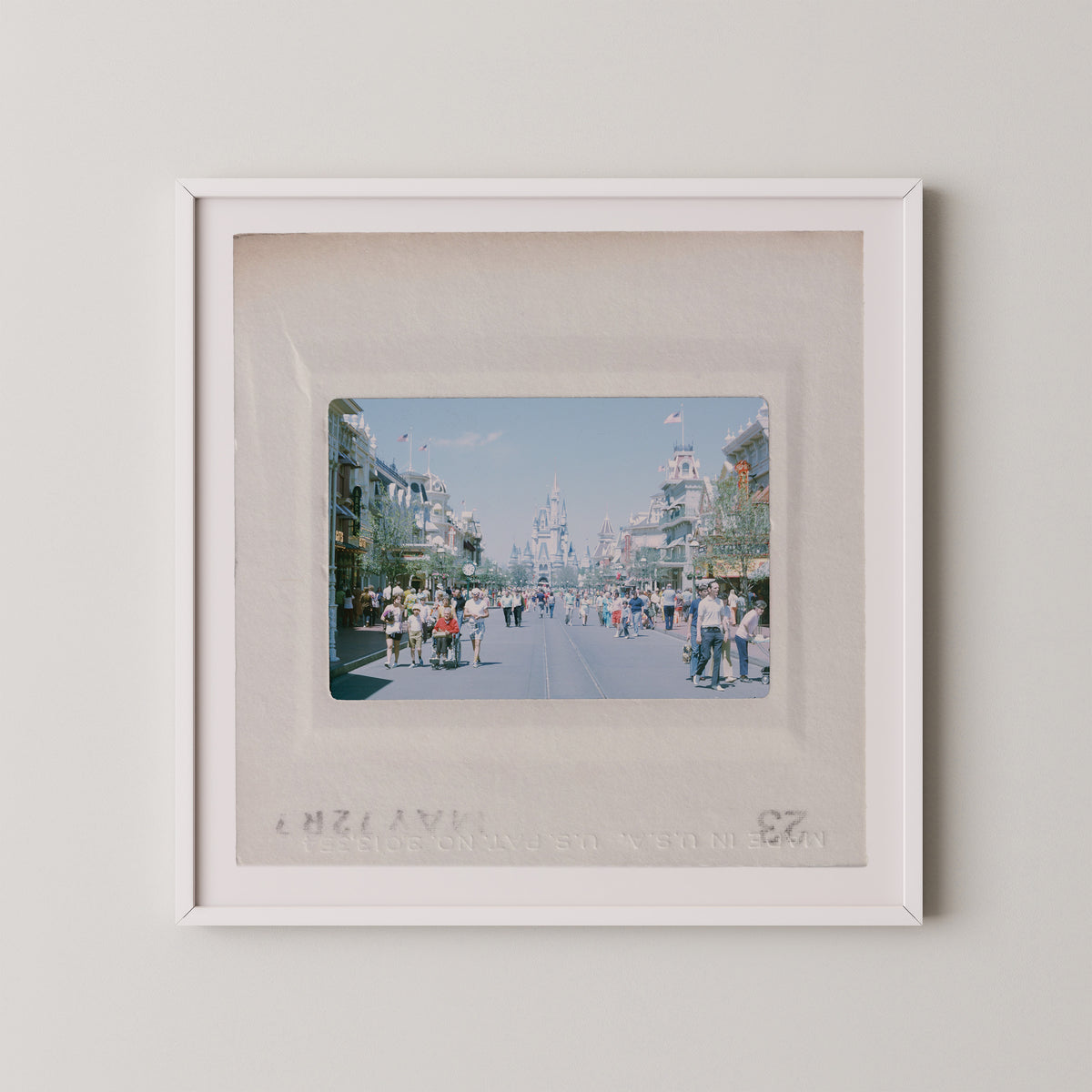 The image is a framed photograph of a busy street scene with people walking and standing on the sidewalk.