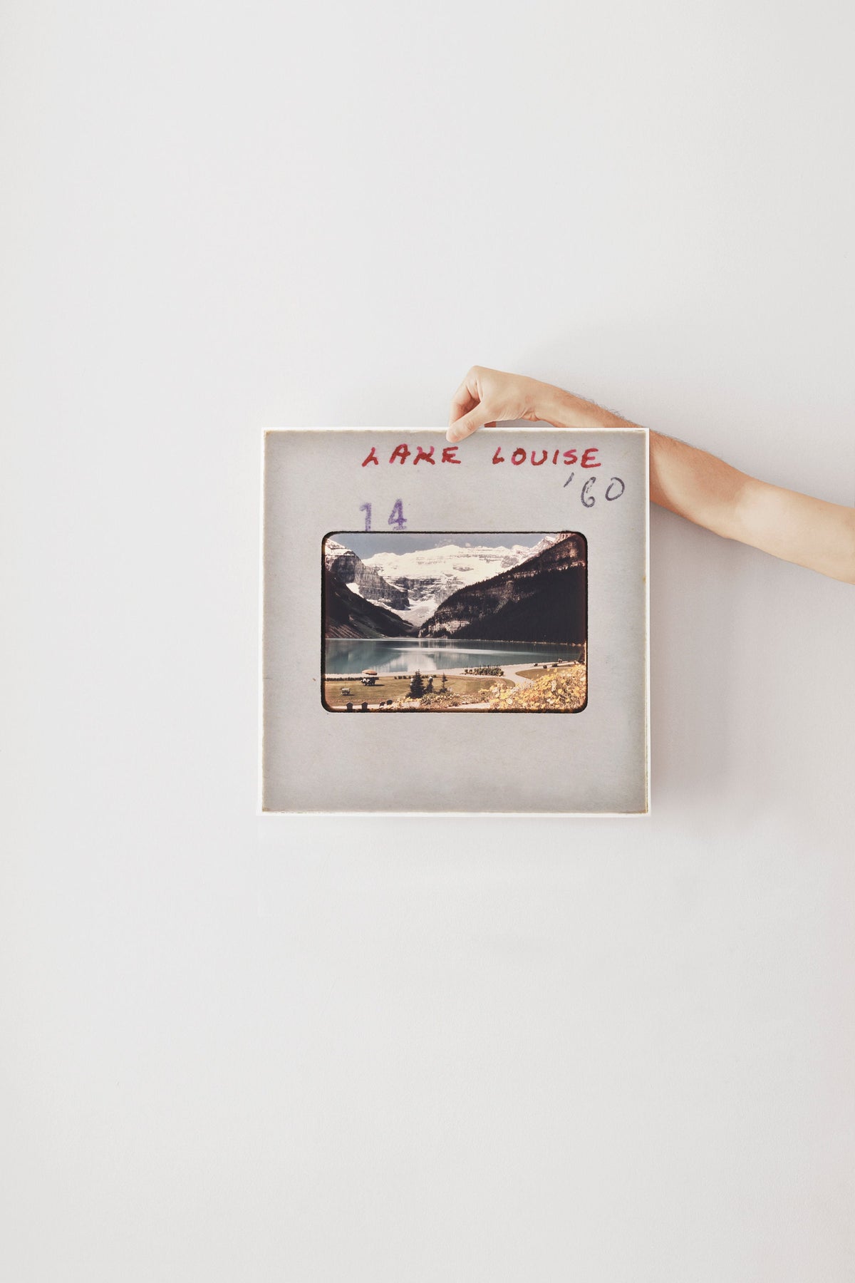 A person's hand is holding a framed photograph of a mountain landscape, with the text "Able Louise '60" written on the frame.