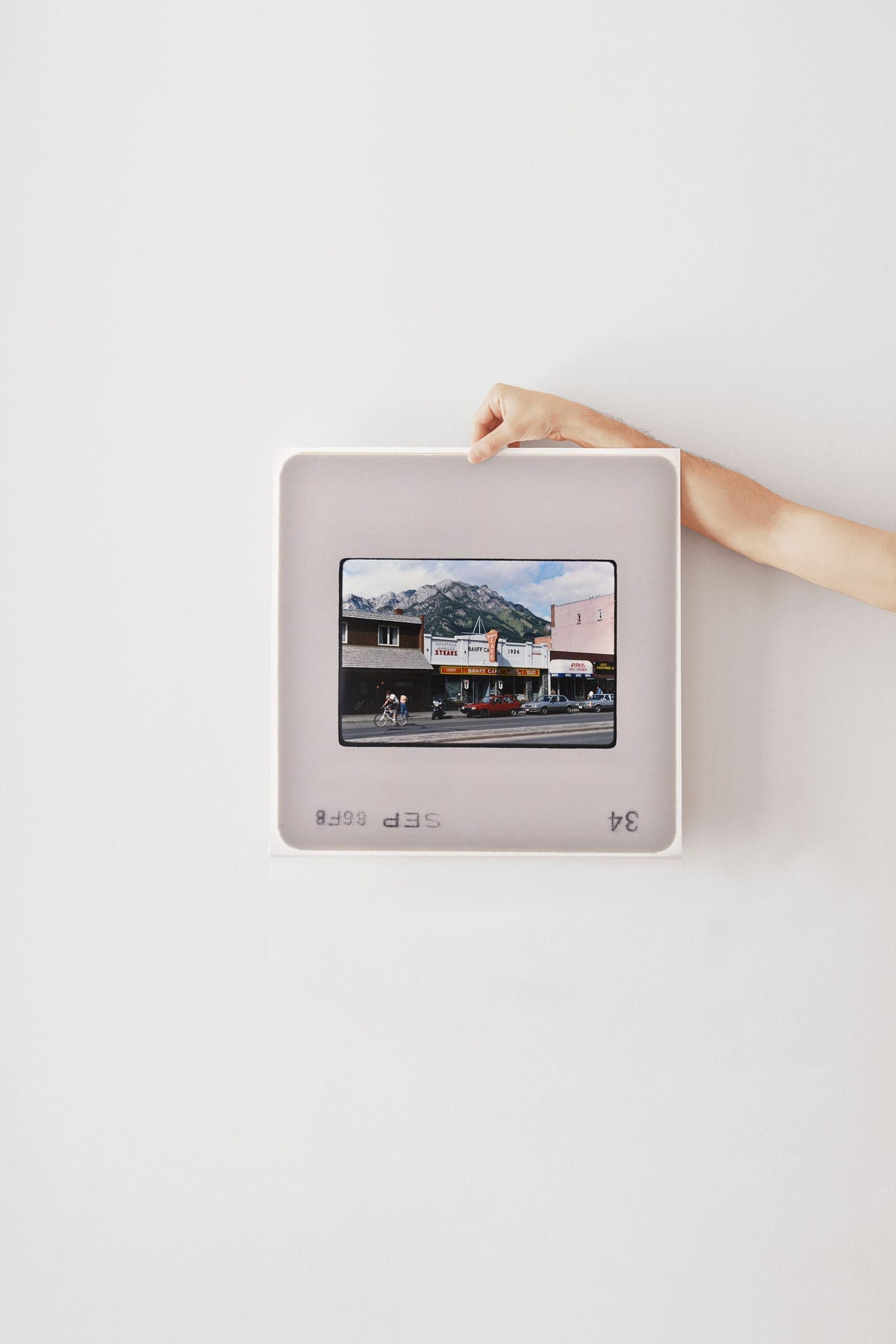 A person's hand is holding a framed photograph of a building with a mountain in the background.