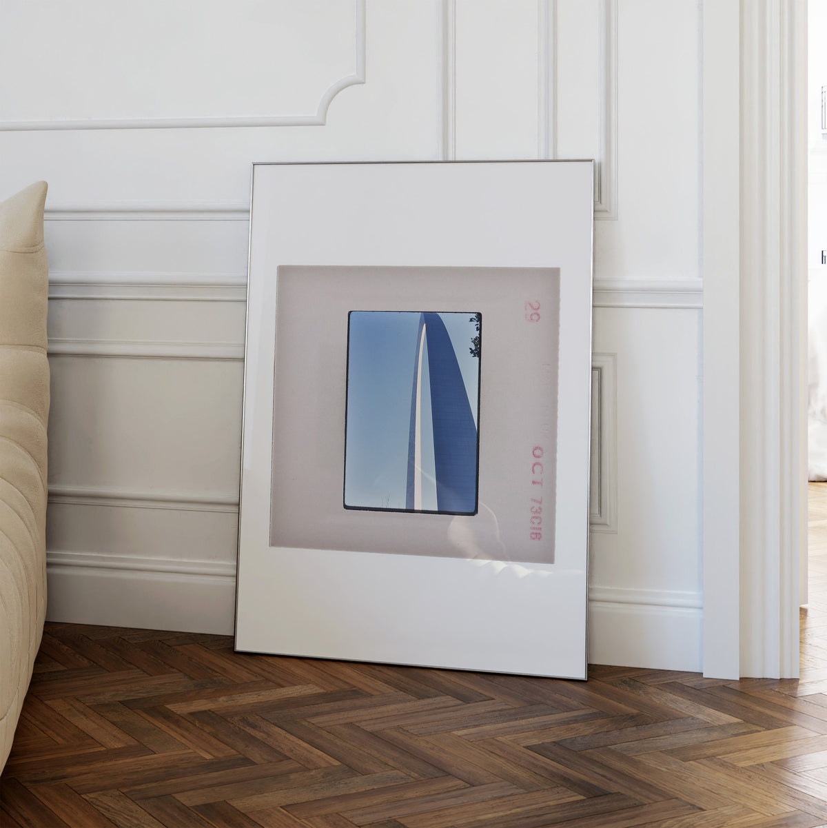 a white picture frame with a square photograph of a sailboat on a blue background, placed on a wooden floor against a white wall.