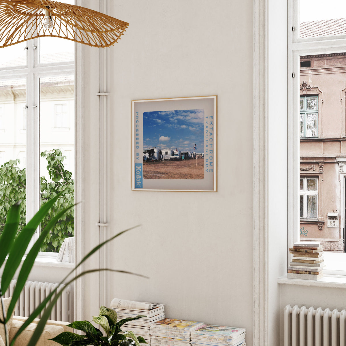 a framed photograph of a beach scene hanging on a wall, with a window and a plant visible in the foreground.