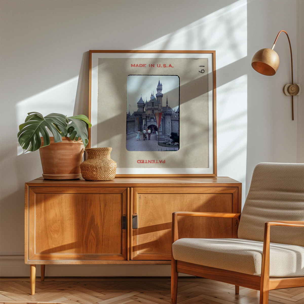 a framed picture of a castle, a potted plant, a wooden cabinet, and a chair in a room with sunlight streaming in.