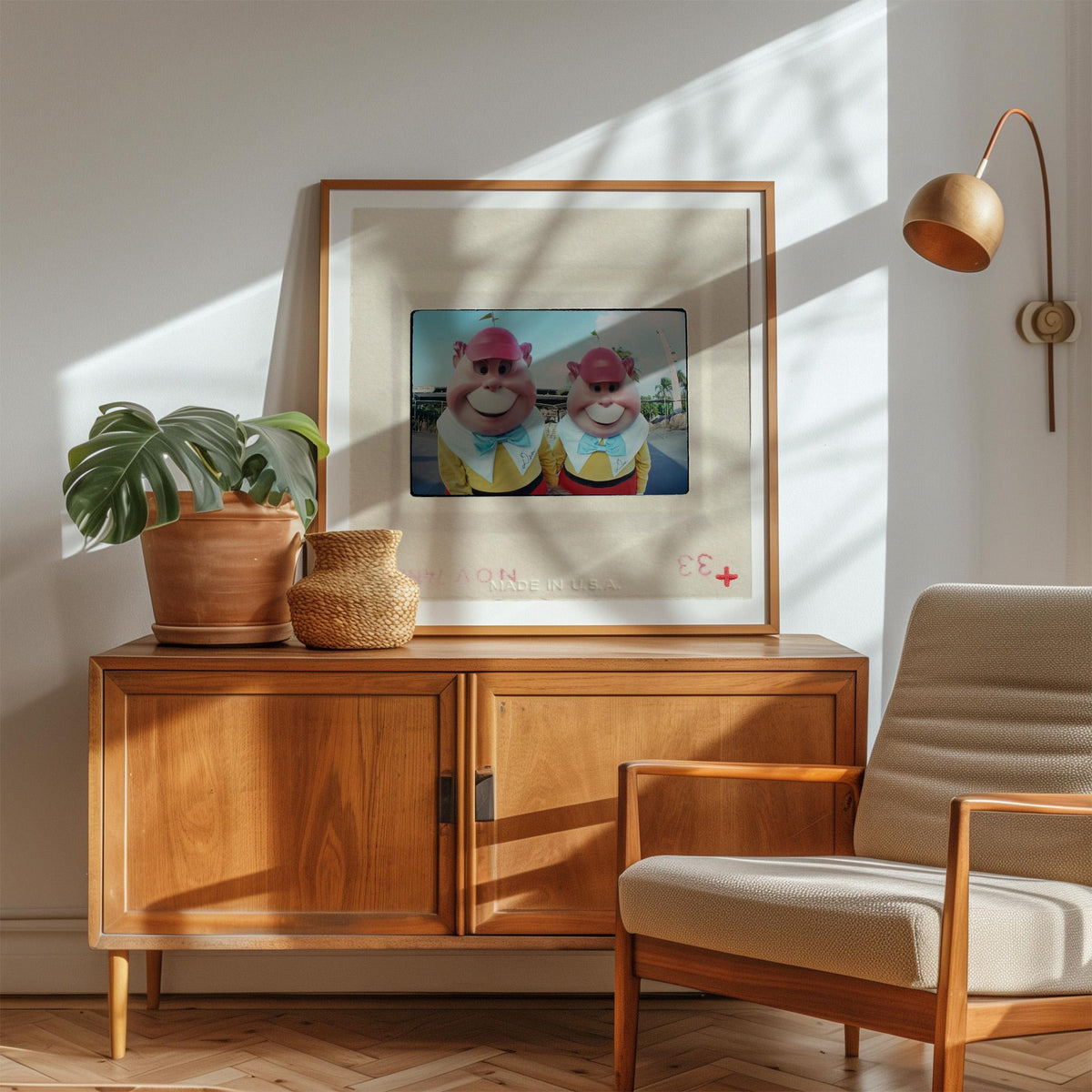 a wooden cabinet with a framed photo of two cartoon characters on top, a potted plant, and a woven basket on the cabinet. There is also a beige armchair in the foreground.