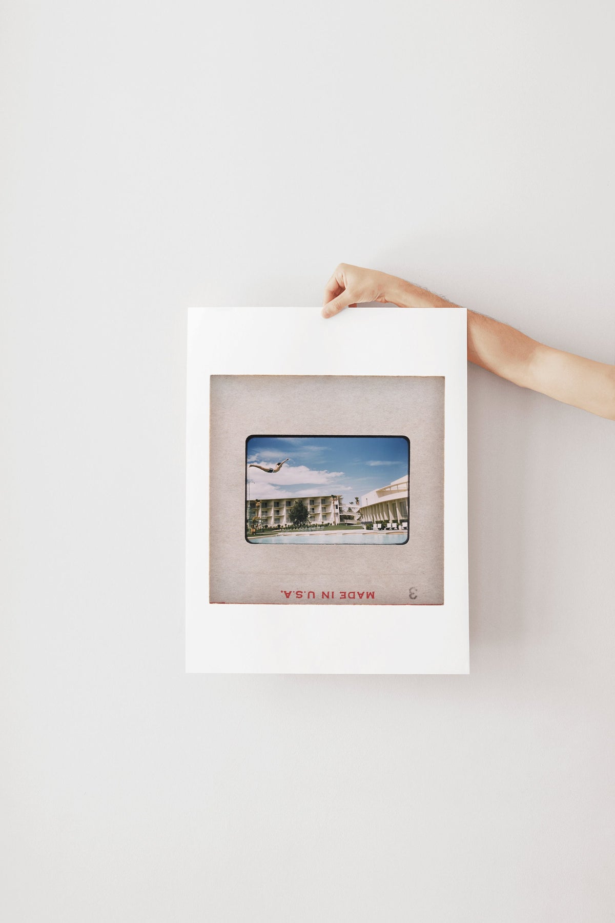 A person's hand is holding a framed photograph of a building with a plane flying overhead.