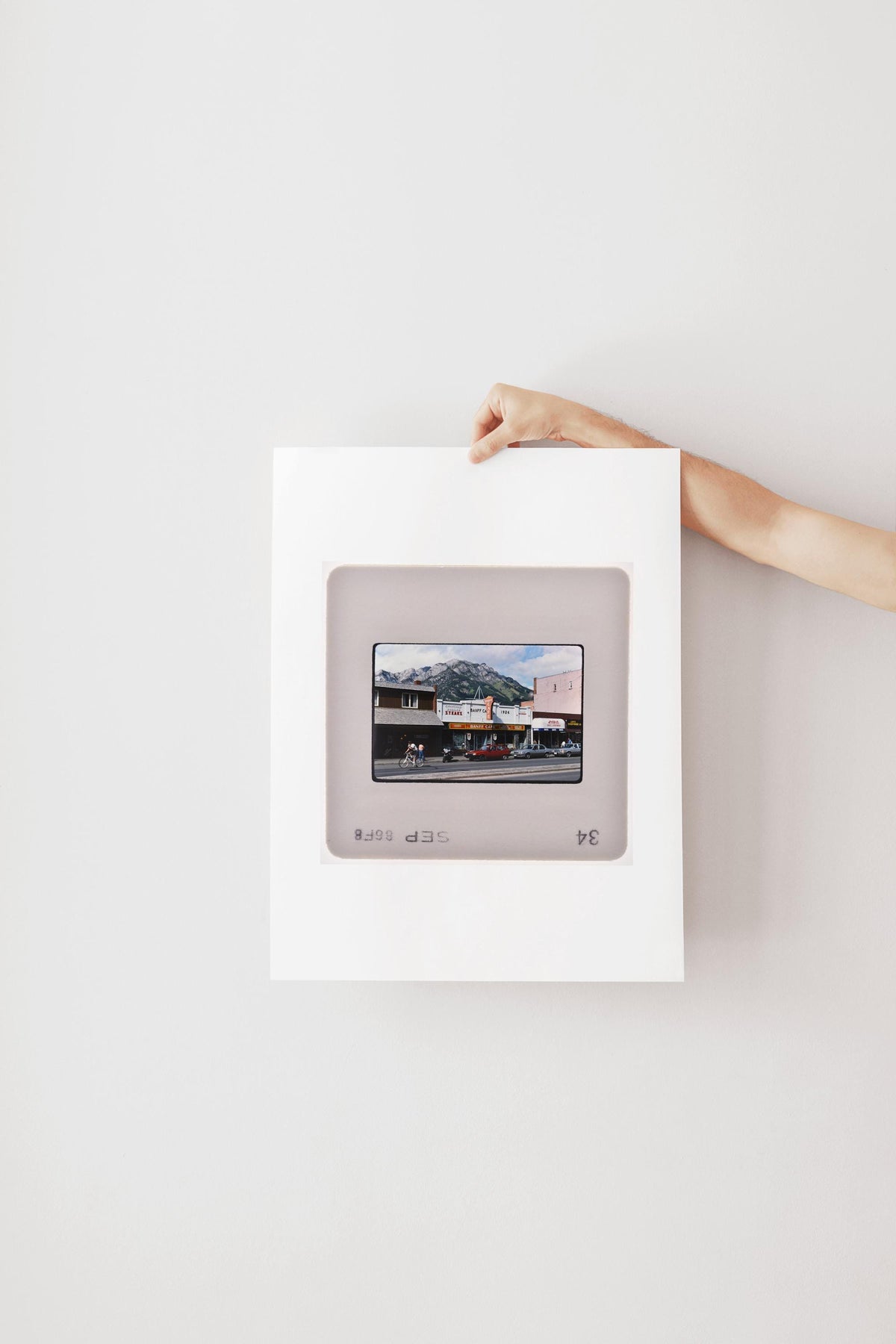 A person's hand is holding a framed photograph of a building with a mountain in the background.