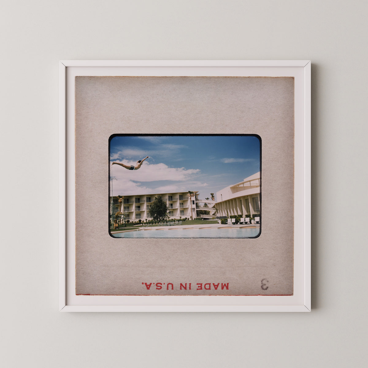 A framed photograph of a person diving off a diving board at a pool, with a hotel building visible in the background.