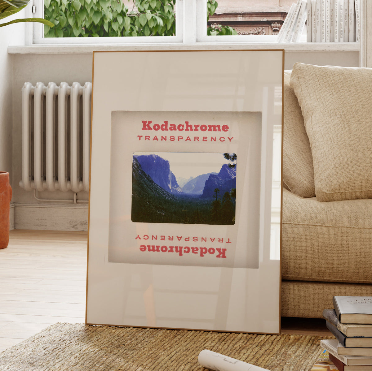 A framed photograph of a mountainous landscape is displayed on a wooden floor in a living room.
