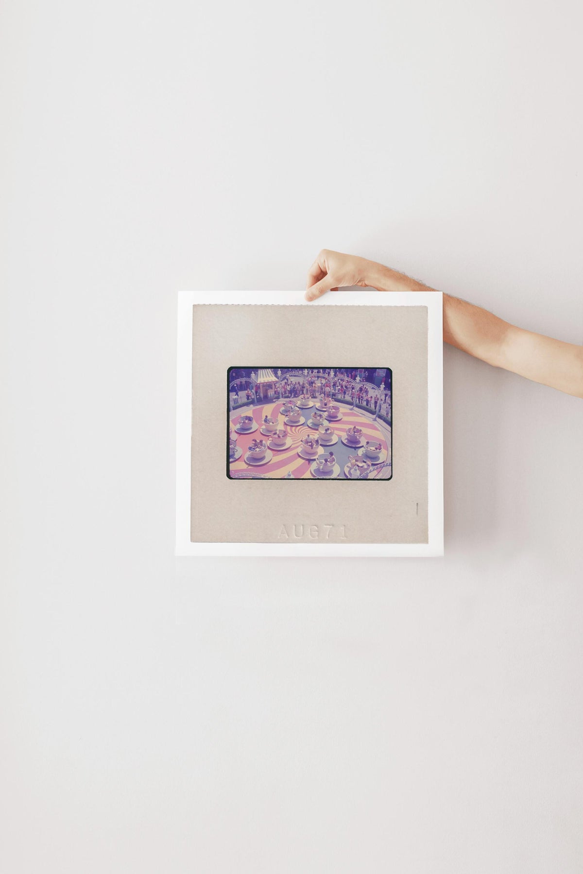 A person's hand is holding a framed picture of a colorful, abstract image on a white wall.