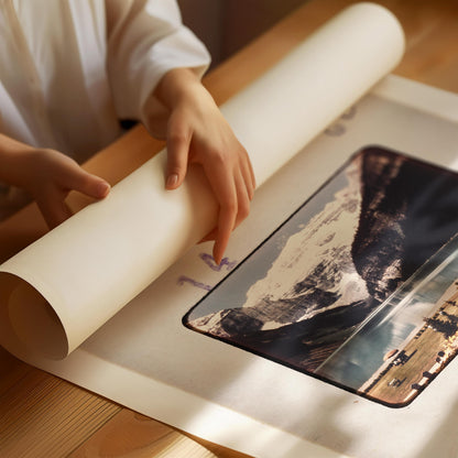 A person's hands are holding a roll of paper, which appears to be a canvas or paper for painting or drawing. The image features a landscape scene with mountains and a body of water, suggesting it could be a painting or drawing of a natural landscape.