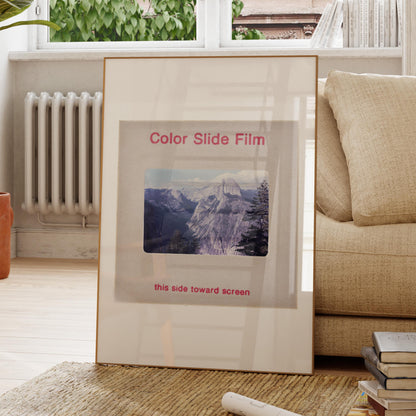 a framed photograph of a mountain landscape, placed on a wooden floor in a living room setting.