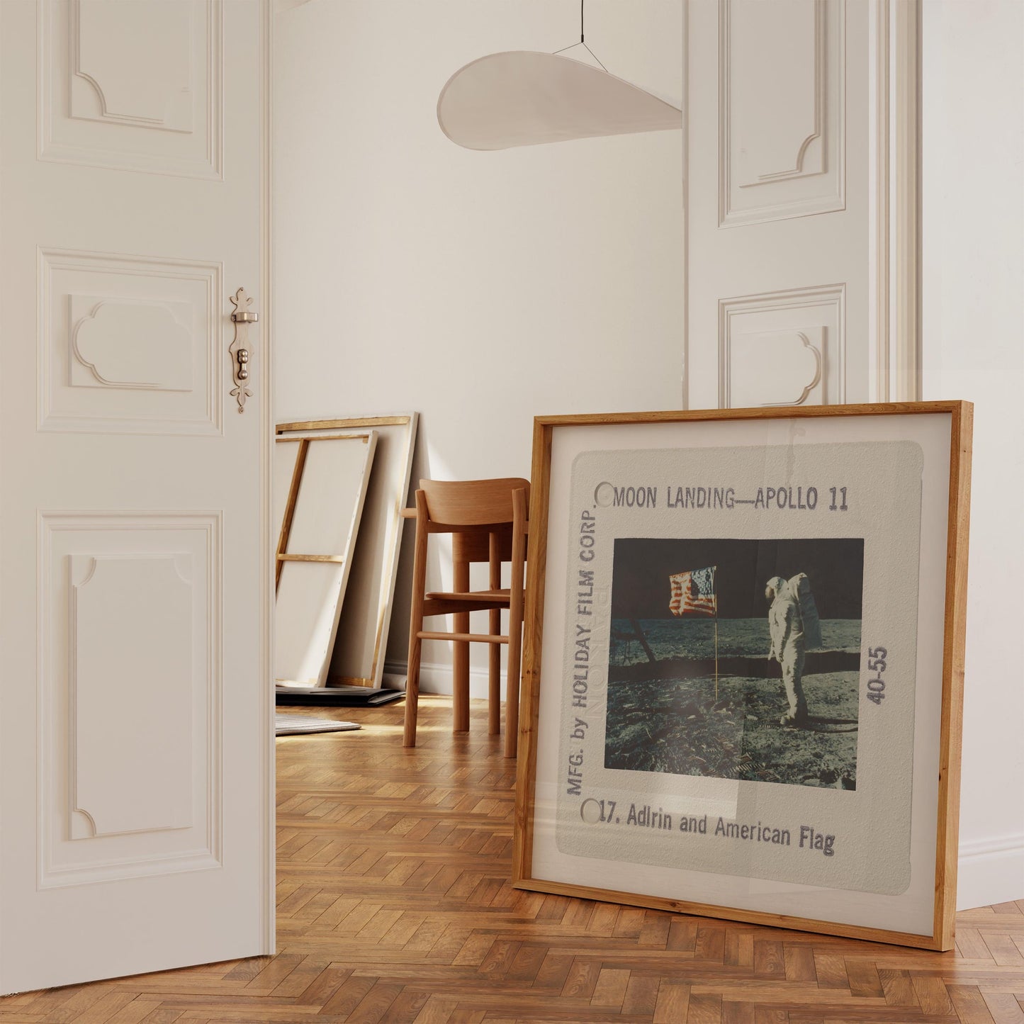 a framed photograph of the Apollo 11 moon landing, with a chair and a painting in the background.