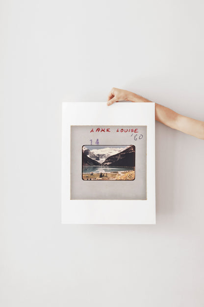A person's hand is holding a framed photograph of a mountain landscape.