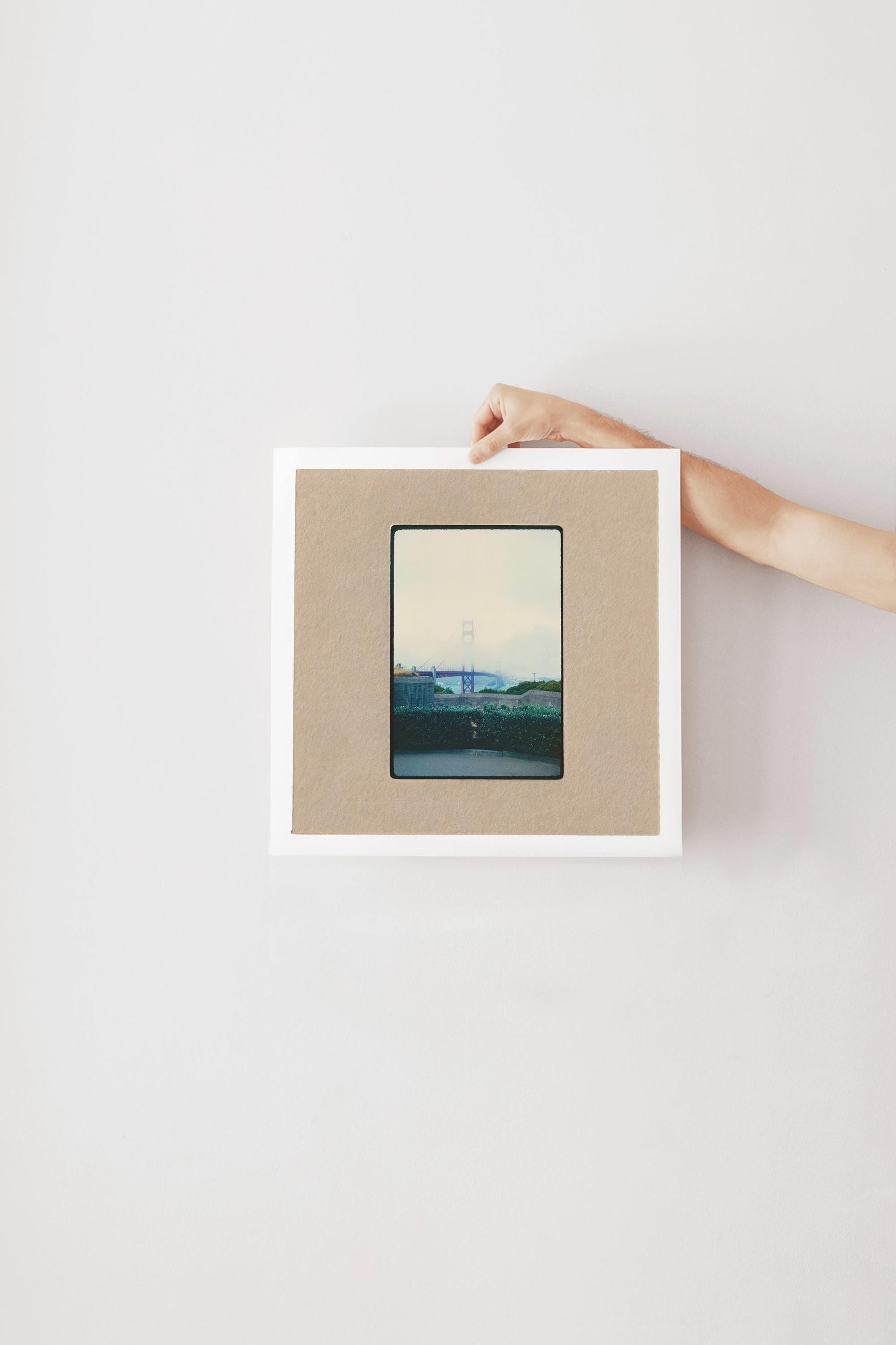 Vintage 35mm slide photograph of the Golden Gate Bridge partially obscured by dense fog, with only the tower visible above the cloud layer, viewed from a concrete overlook with green hedges in the foreground. Printed as a giclée fine art print on archival matte paper.