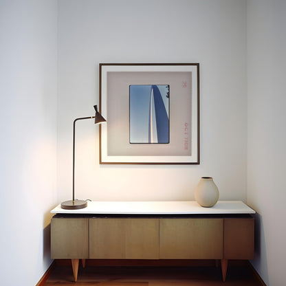 a minimalist corner of a room with a wooden cabinet, a lamp, and a framed artwork on the wall.