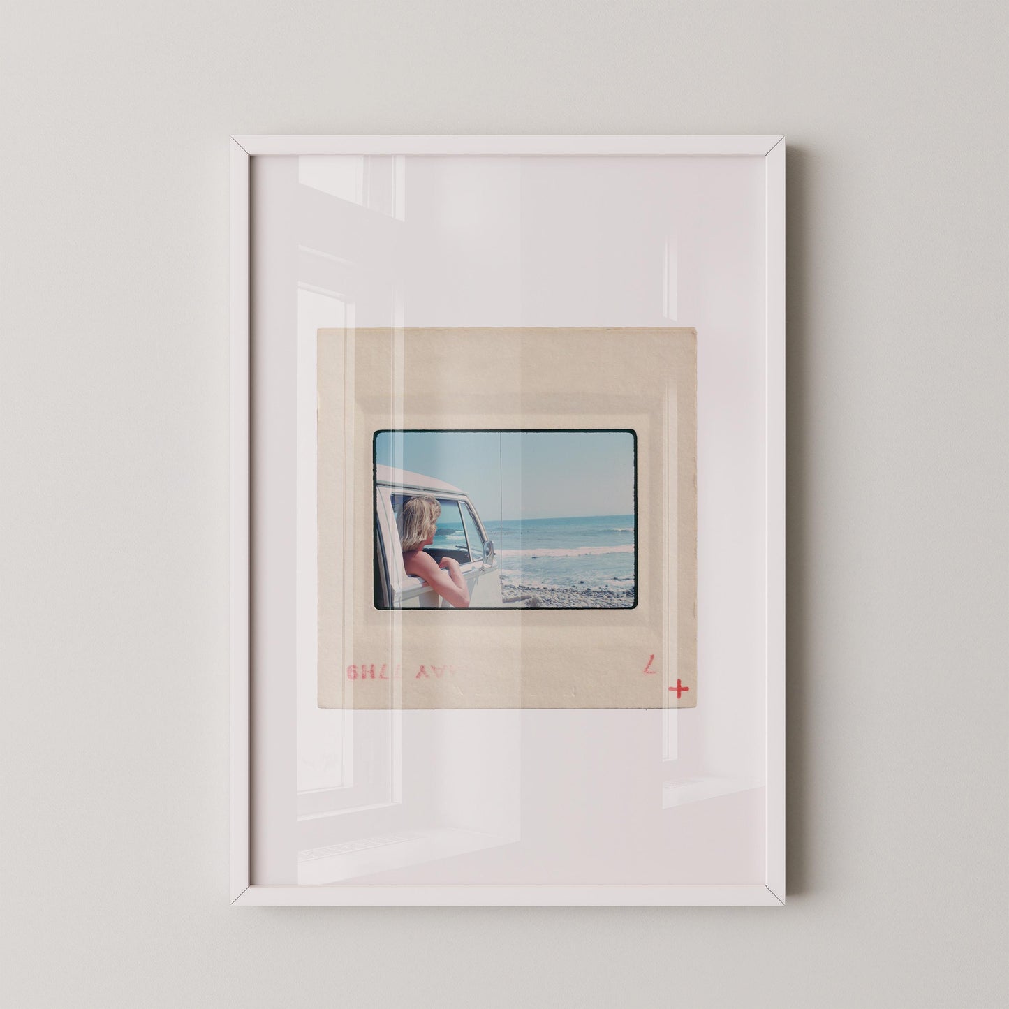Vintage 1977 Kodachrome slide photograph of a blonde child leaning out the window of a white Volkswagen Microbus, looking toward the ocean along the California coast. Rocky shoreline and gentle surf visible in the background. Printed as a giclée fine art print on archival matte paper.