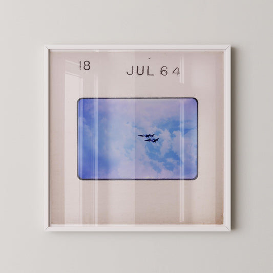 The image is a framed photograph of a plane flying in the sky, with the date "JUL 64" displayed above it.