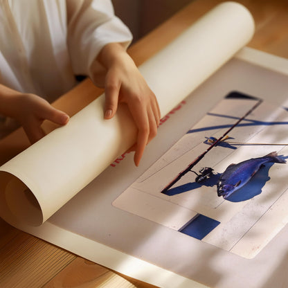 A person's hands are holding a roll of paper, which appears to be a canvas or paper for painting or drawing. The person is sitting at a table, focused on the artwork displayed on the paper.