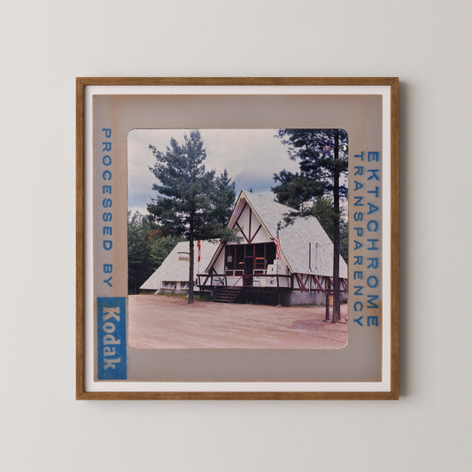 A framed photograph of a white triangular building with a red roof, surrounded by trees, with the text "Kodak" visible in the frame.