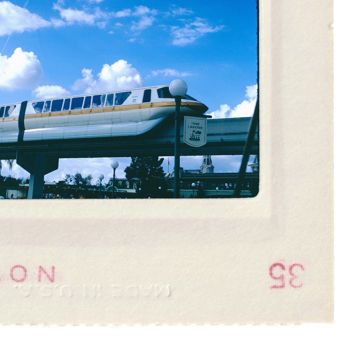 A monorail train is shown traveling over a bridge, with a clear blue sky and clouds in the background.