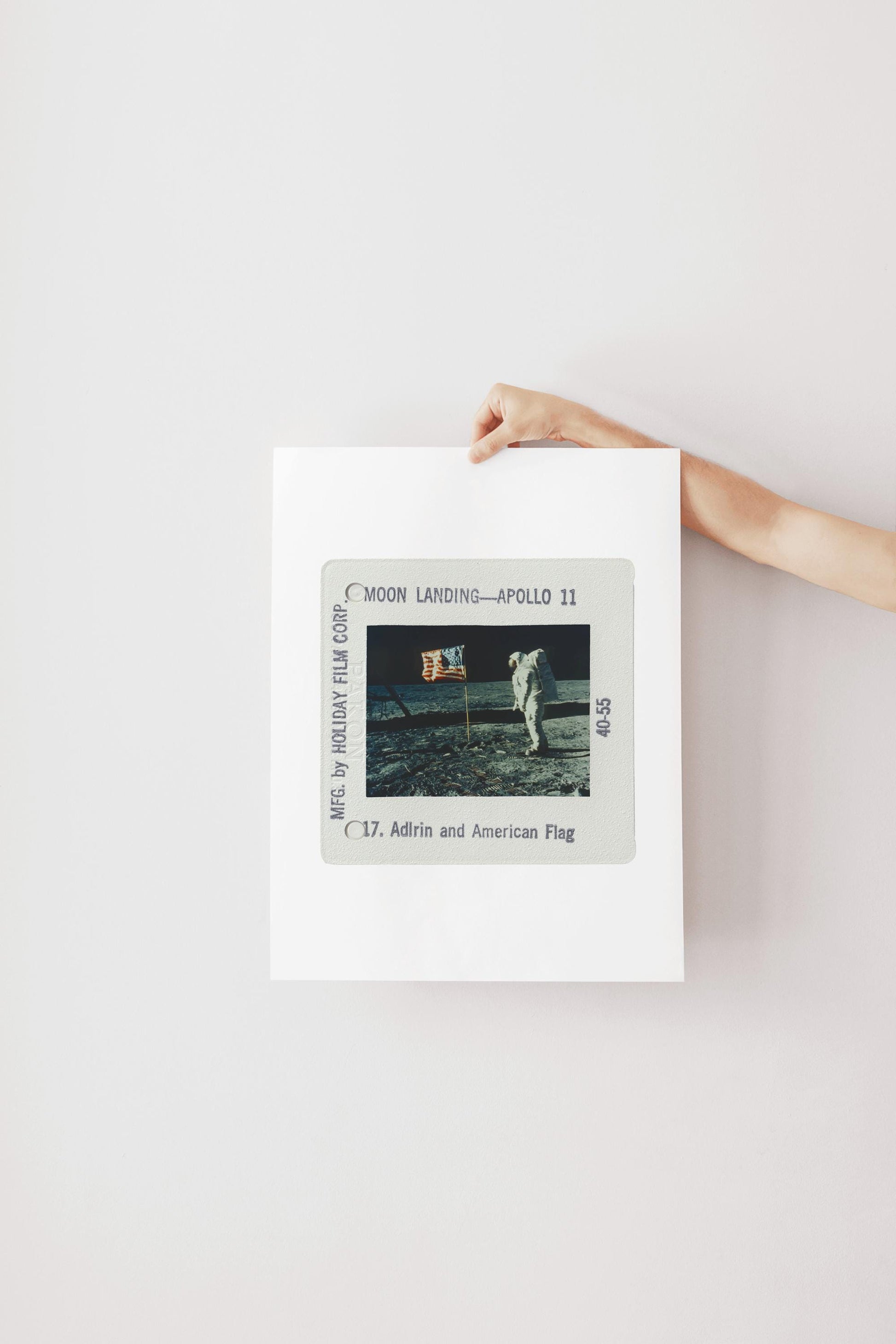 A person's hand is holding a framed photograph of the Apollo 11 moon landing, with the text "Moon Landing—Apollo 11" visible.