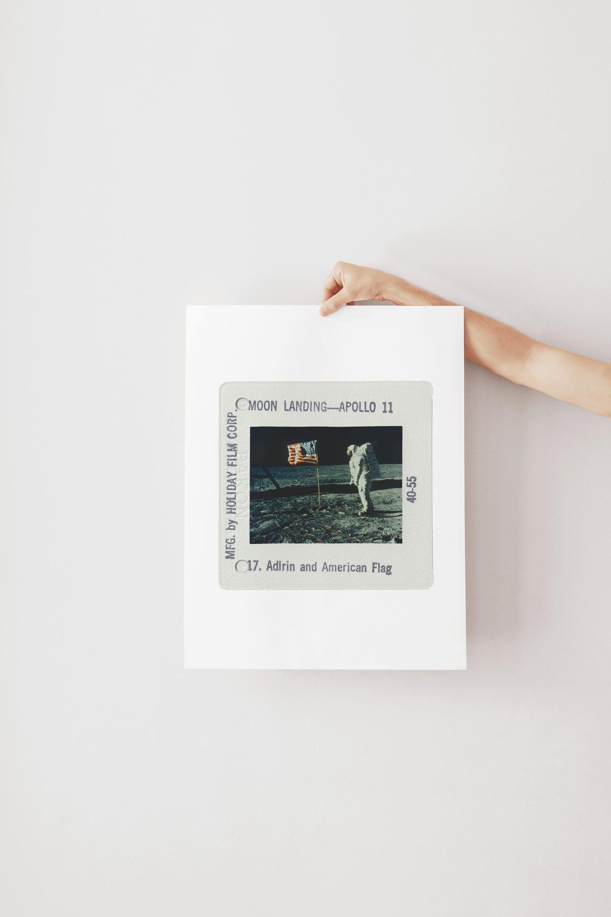 A person's hand is holding a framed photograph of the Apollo 11 moon landing, with the text "Moon Landing—Apollo 11" visible.