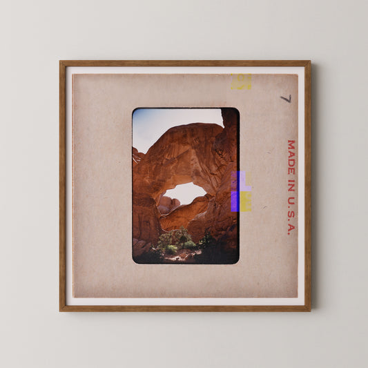 The image is a framed photograph of a desert landscape with a large rock formation, likely a canyon or arch, in the background.