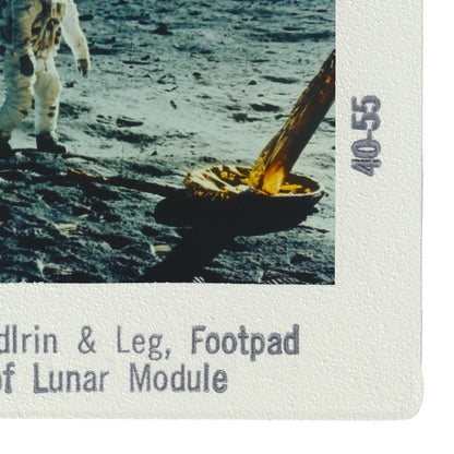 a person walking on the lunar surface, with a large object, possibly a tool or equipment, in their hand.