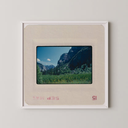 The image is a framed photograph of a mountainous landscape with a clear blue sky and lush green vegetation.