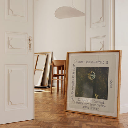 a framed photograph of the Apollo 11 moon landing, with a wooden chair and a white door visible in the background.