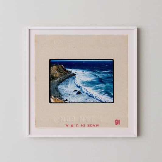 The image is a framed photograph of a rocky coastline with crashing waves, depicting a scenic coastal landscape.