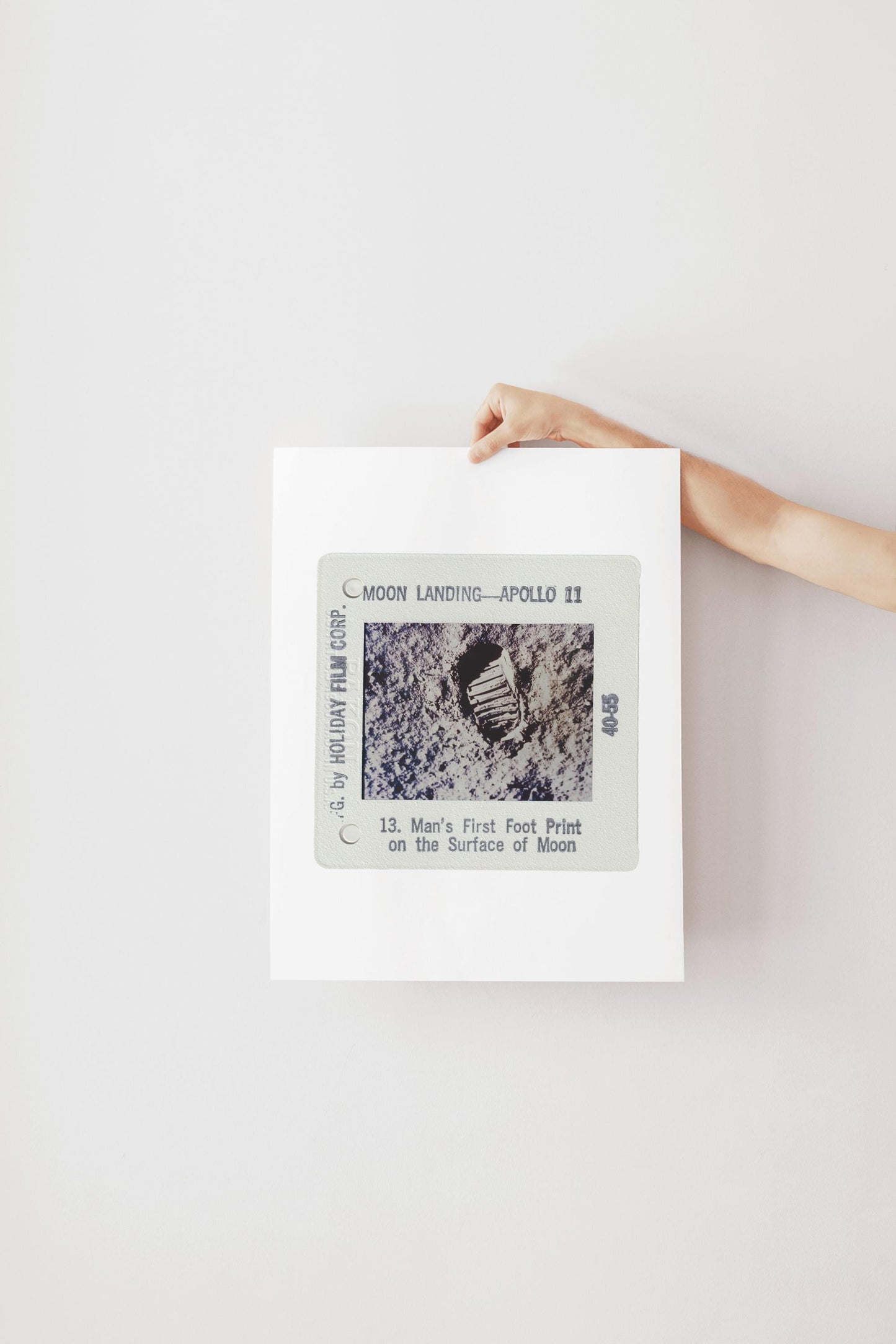 A person's hand is holding a framed photograph of the Apollo 11 moon landing, featuring the first footprint on the surface of the moon.