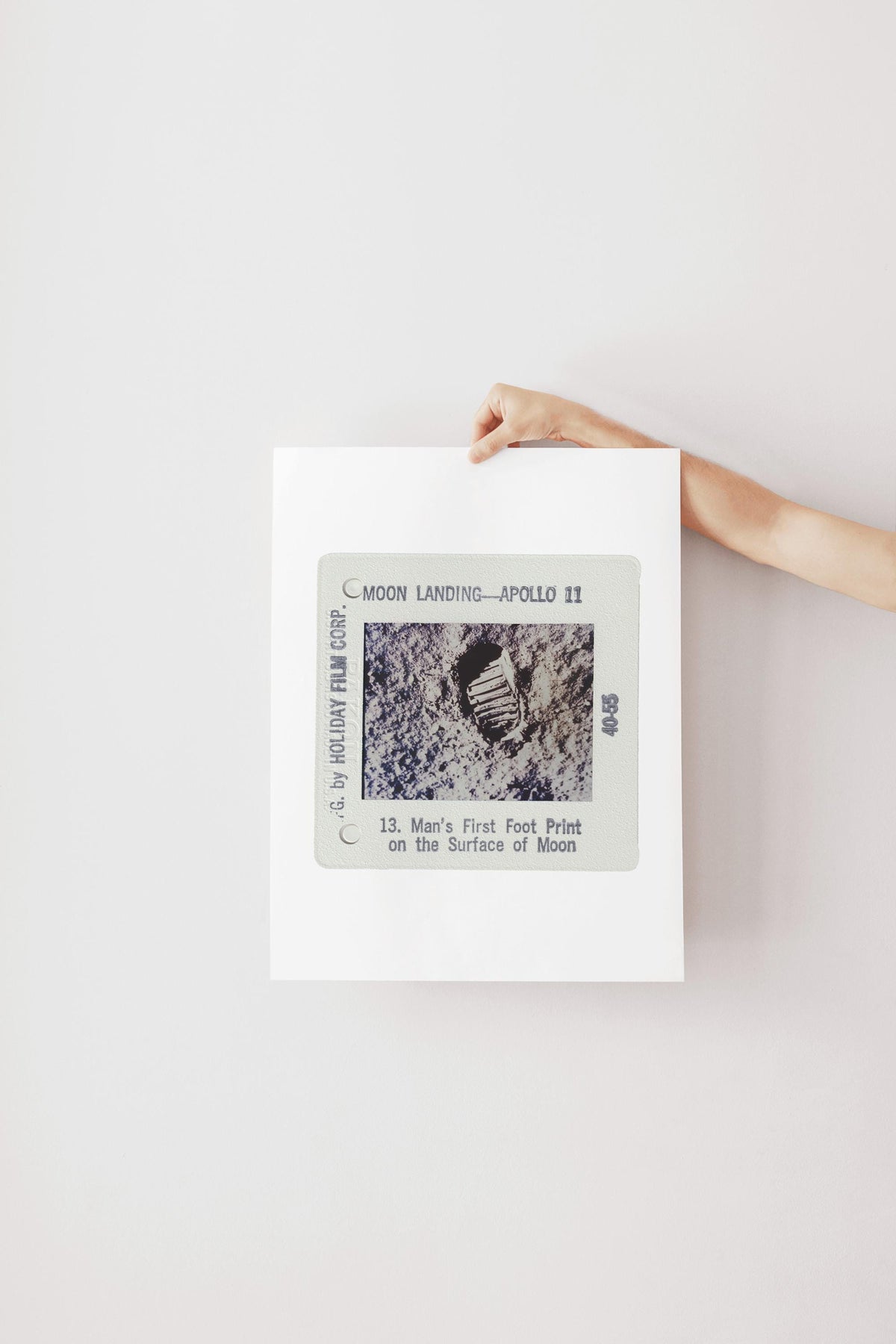 A person's hand is holding a framed photograph of the Apollo 11 moon landing, featuring the first footprint on the surface of the moon.