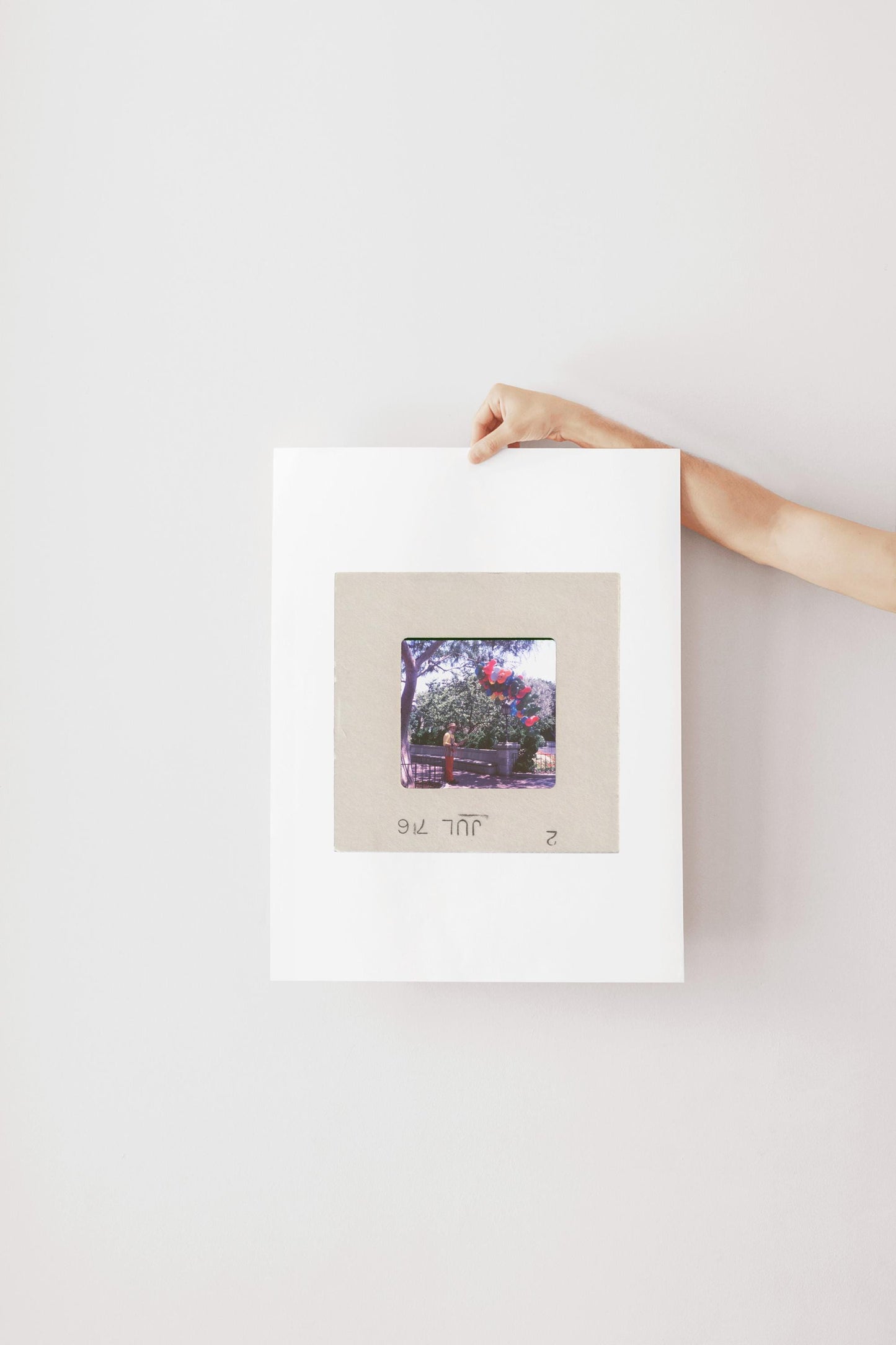 A hand is holding a white piece of paper with a framed photograph of a person standing in front of a tree.