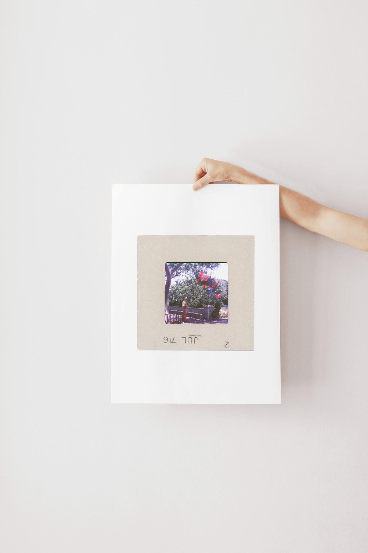 A hand is holding a white piece of paper with a framed photograph of a person standing in front of a tree.