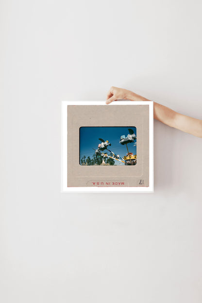 A person's hand is holding a framed picture of a blue sky with a white airplane in the distance.