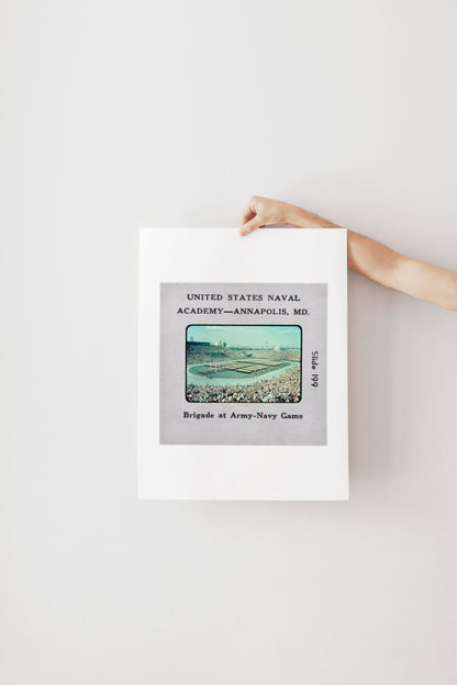 A person's hand is holding a framed photograph of a naval event, specifically the Battle of Annapolis, which took place in the United States Navy Academy in Annapolis, Maryland in July 1999.